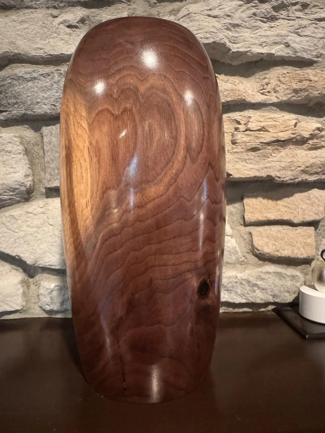 Reverse view of the walnut vase against stone, showing flowing heartwood grain and rounded shoulders