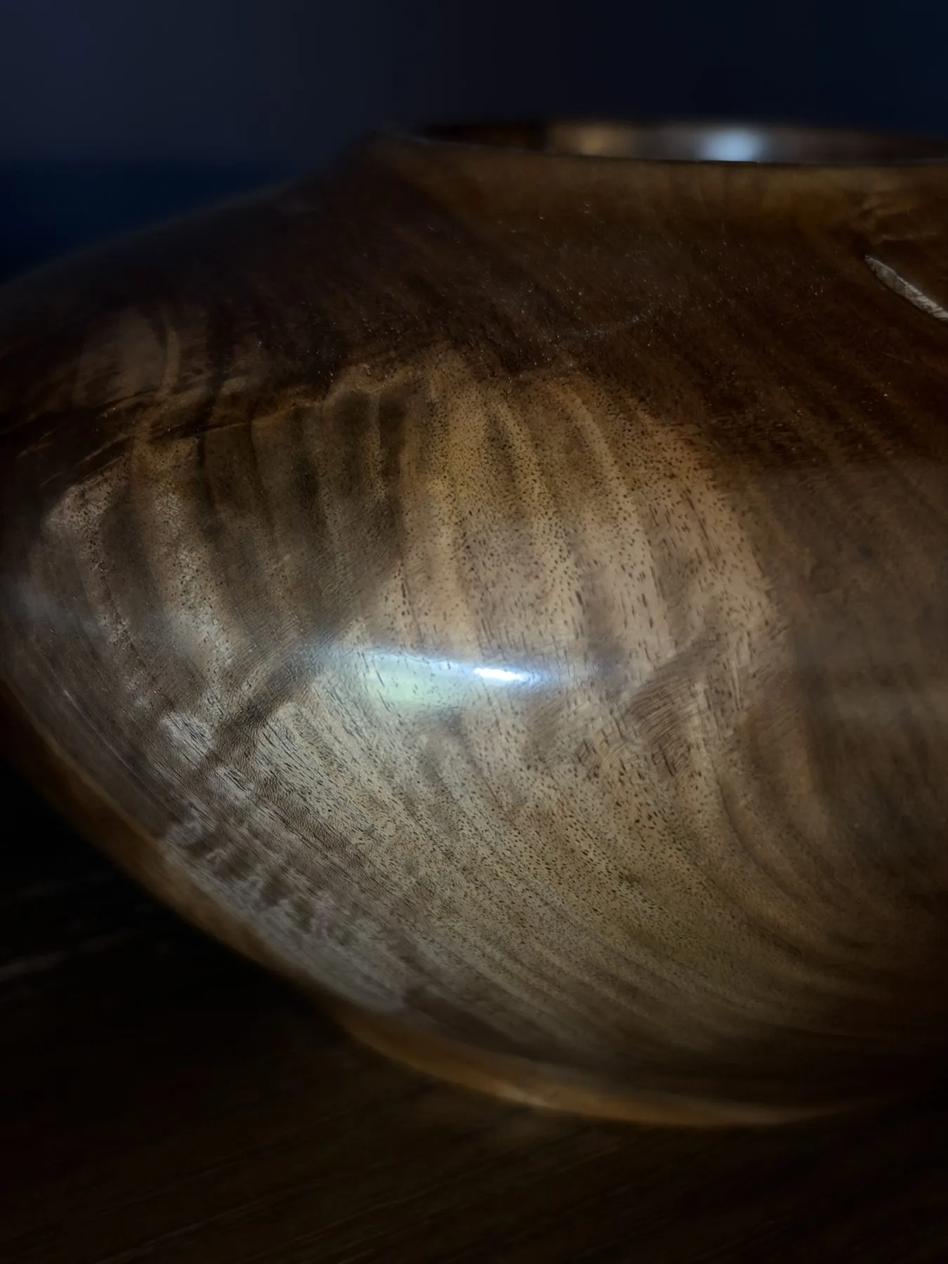 Detail of the walnut surface showing fine pores, rippled grain, and reflected light from the buffed finish
