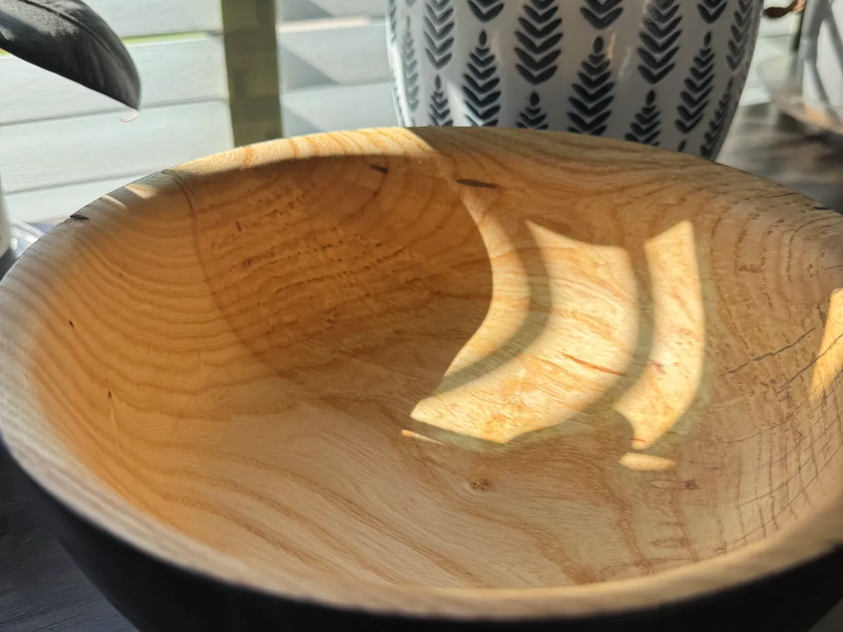 Hand-turned ash wood bowl showing black exterior, natural interior, and open grain texture