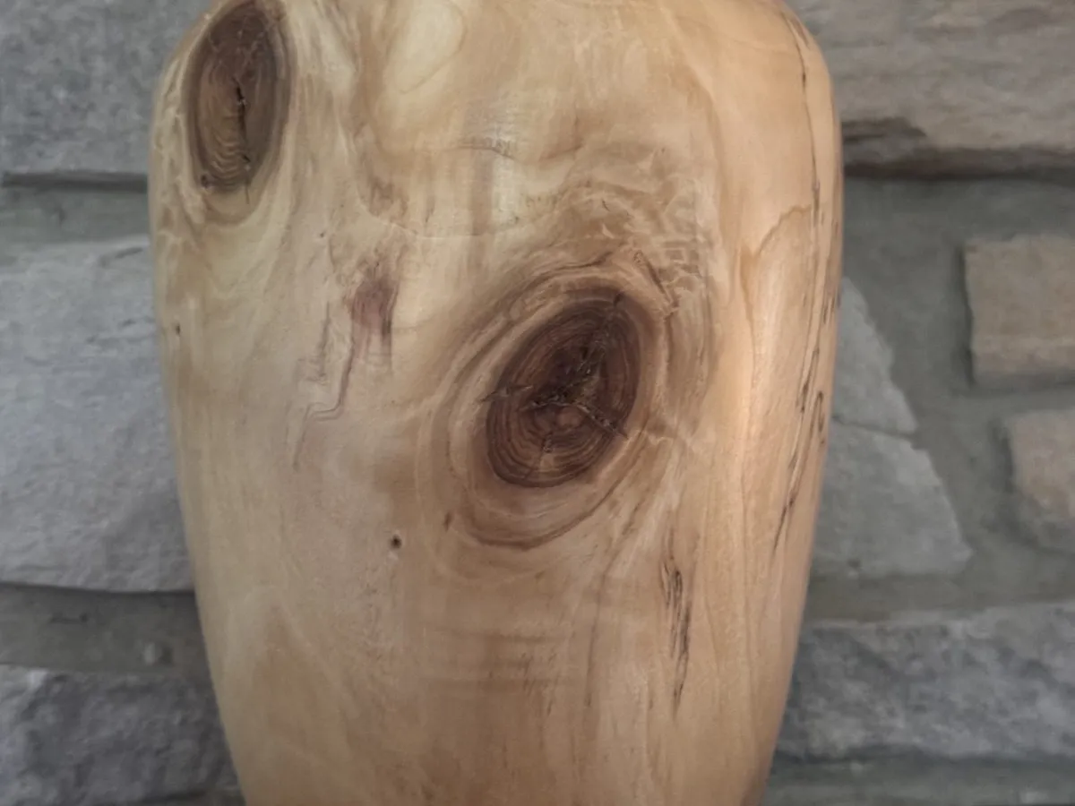 Tall maple vase on a stone background showing a large dark knot eye and pale wood figure
