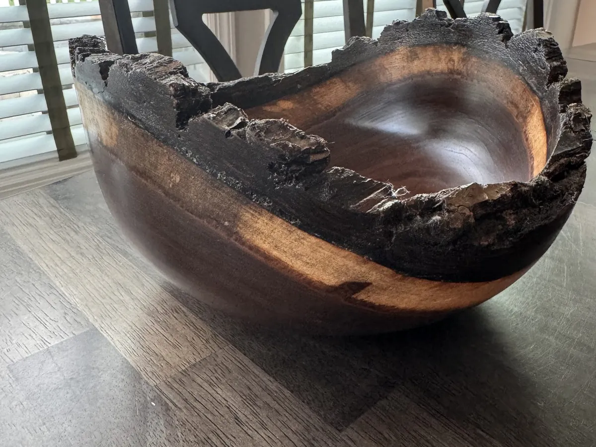 Natural edge walnut bowl displayed on a table with sweeping bark rim