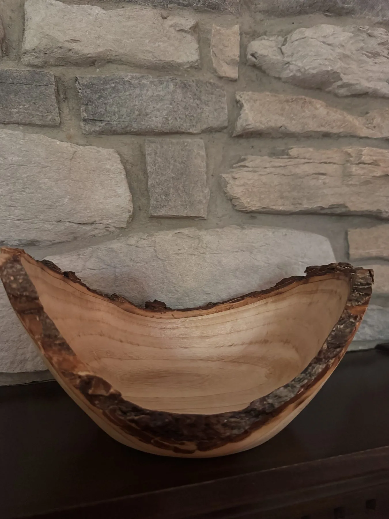 Craggy winged maple bowl displayed on a mantel against a stone background