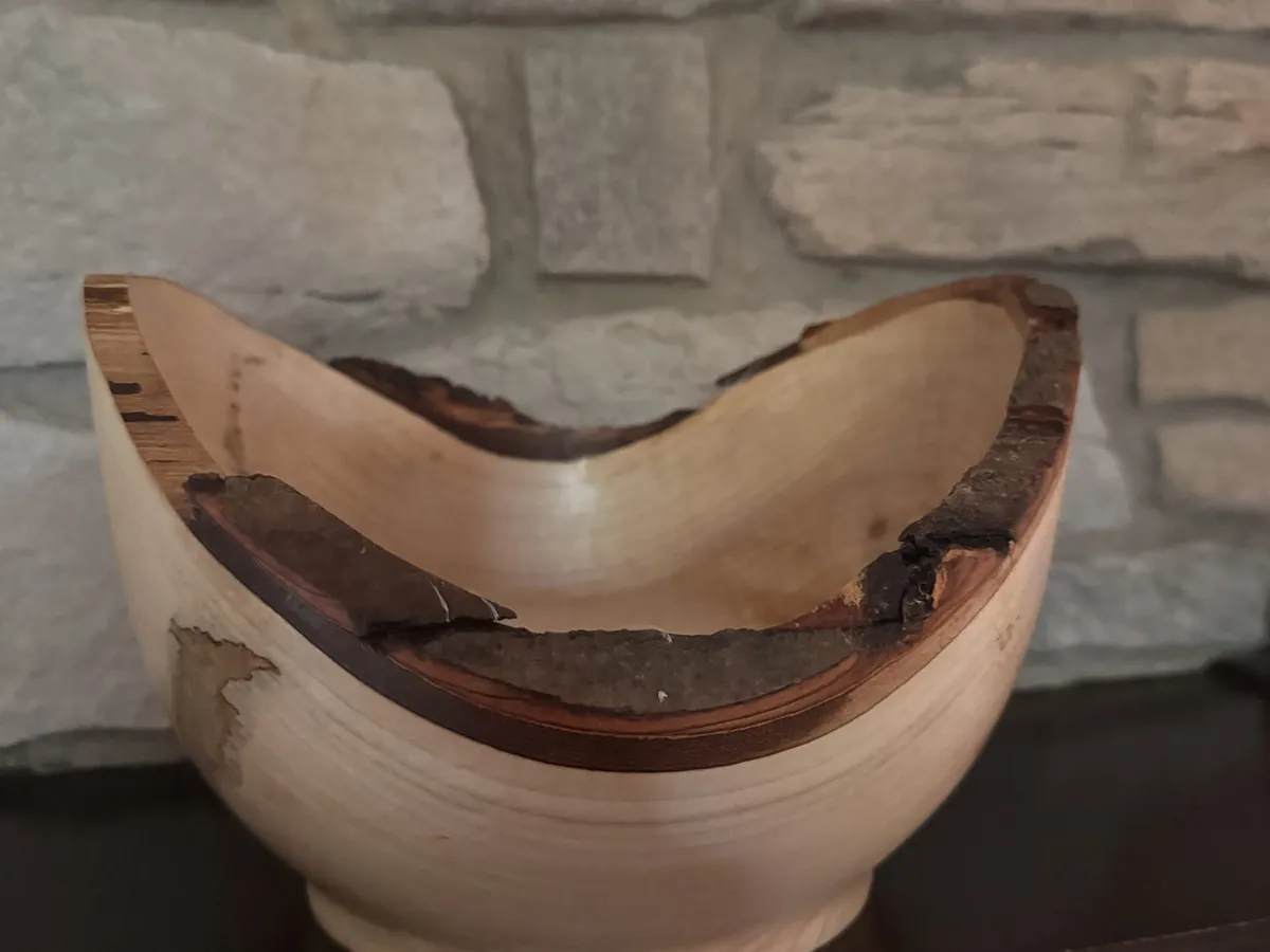 Natural edge maple bowl on a stone background with smooth winged rim and small foot