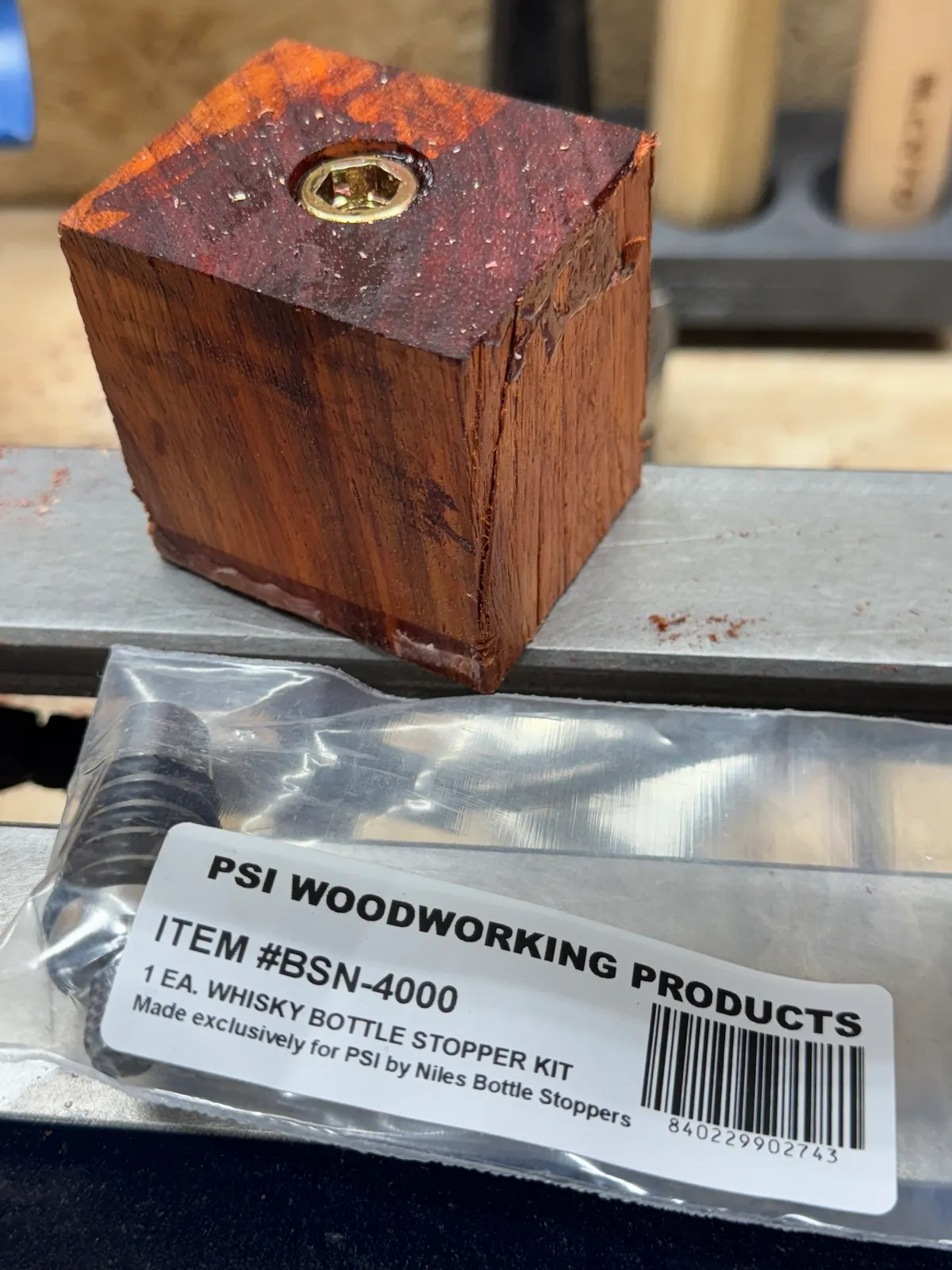A raw padauk blank and a Niles bottle stopper kit package on the lathe